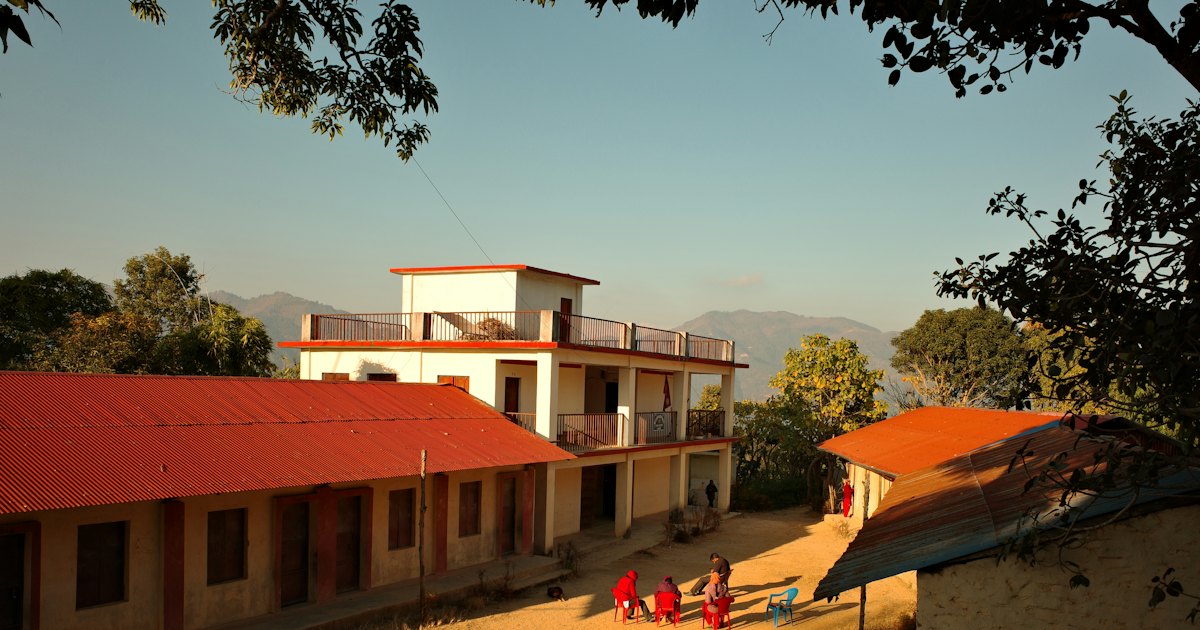 A hillside school in Nepal with red-roofed buildings and children in the courtyard in evening light