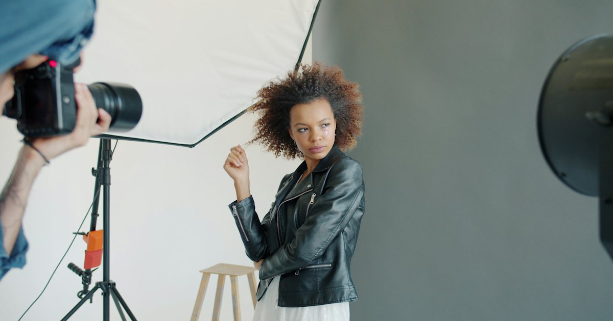 A model posing for a photographer in a studio with softbox lighting and an umbrella reflector