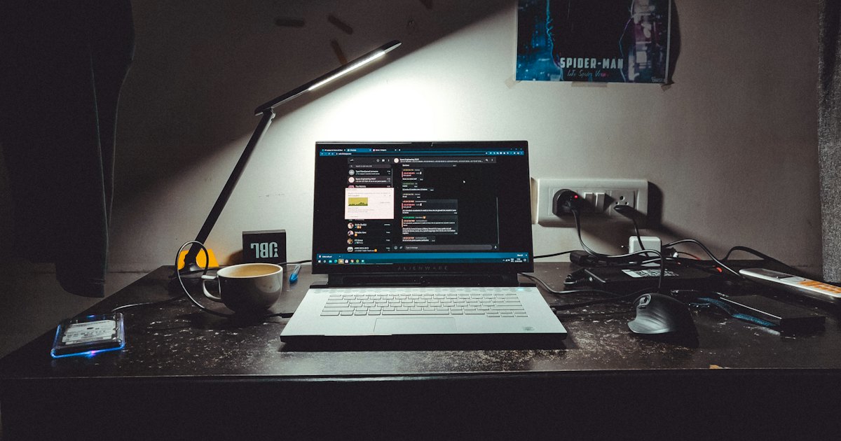 A laptop glowing on a dark desk under a lamp late in the evening