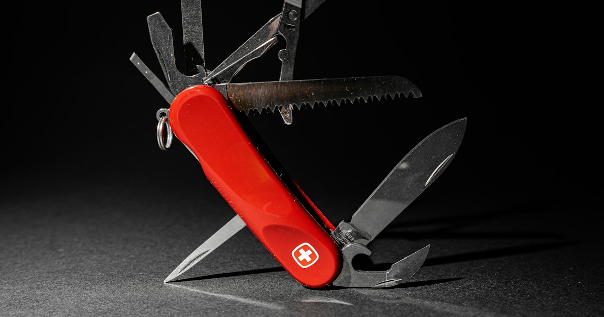 A red Swiss Army knife with several tools extended, photographed against a dark background