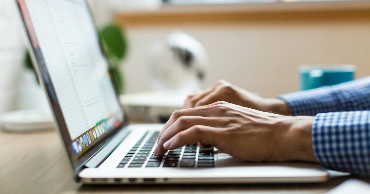 A person's hands typing on a laptop keyboard, side view, with soft natural light from a window