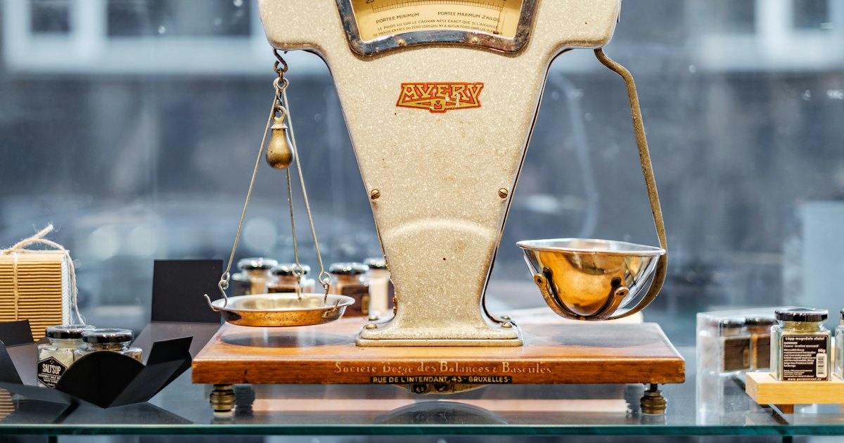 An old brown and beige weighing scale resting on a wooden surface, both pans empty and level