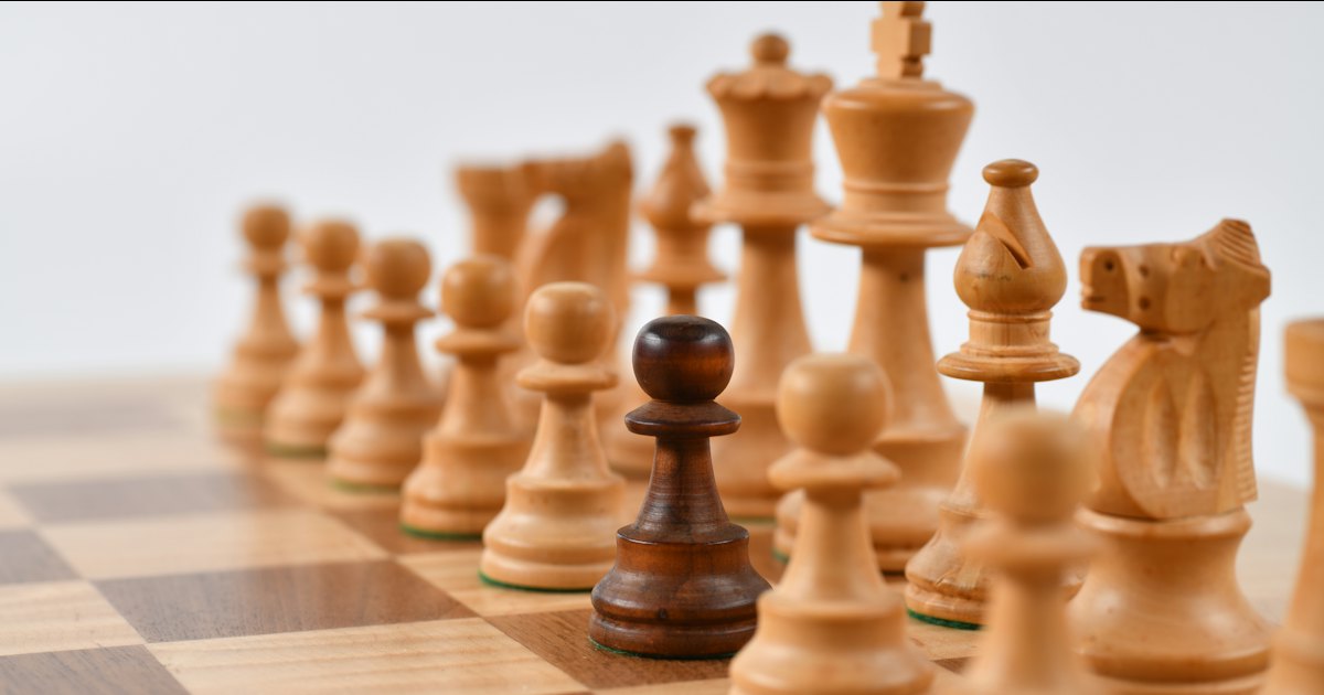 Wooden chess pieces lined up on a board, a dark pawn standing out among the light ones