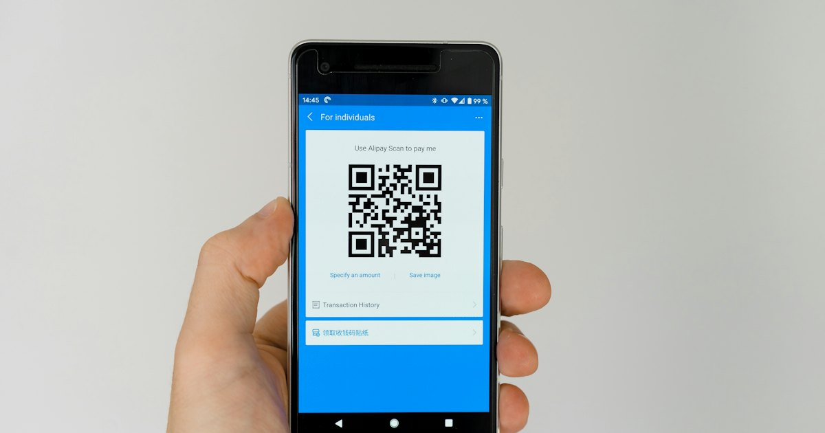 A hand holding a phone that shows a QR payment code on screen
