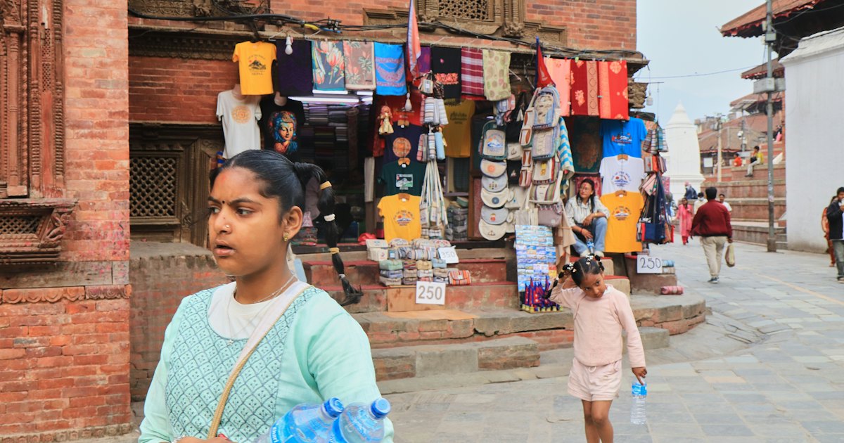 A busy street by Kathmandu Durbar Square with a woman and child walking past a colorful vendor stall