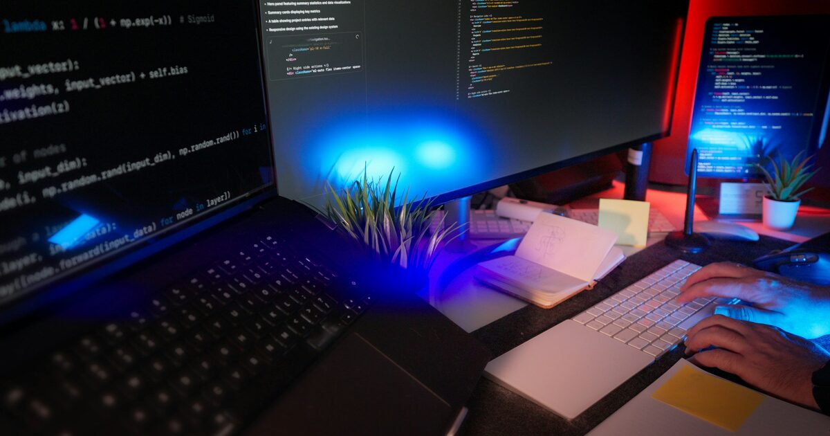 A programmer coding at a desk with several monitors showing code