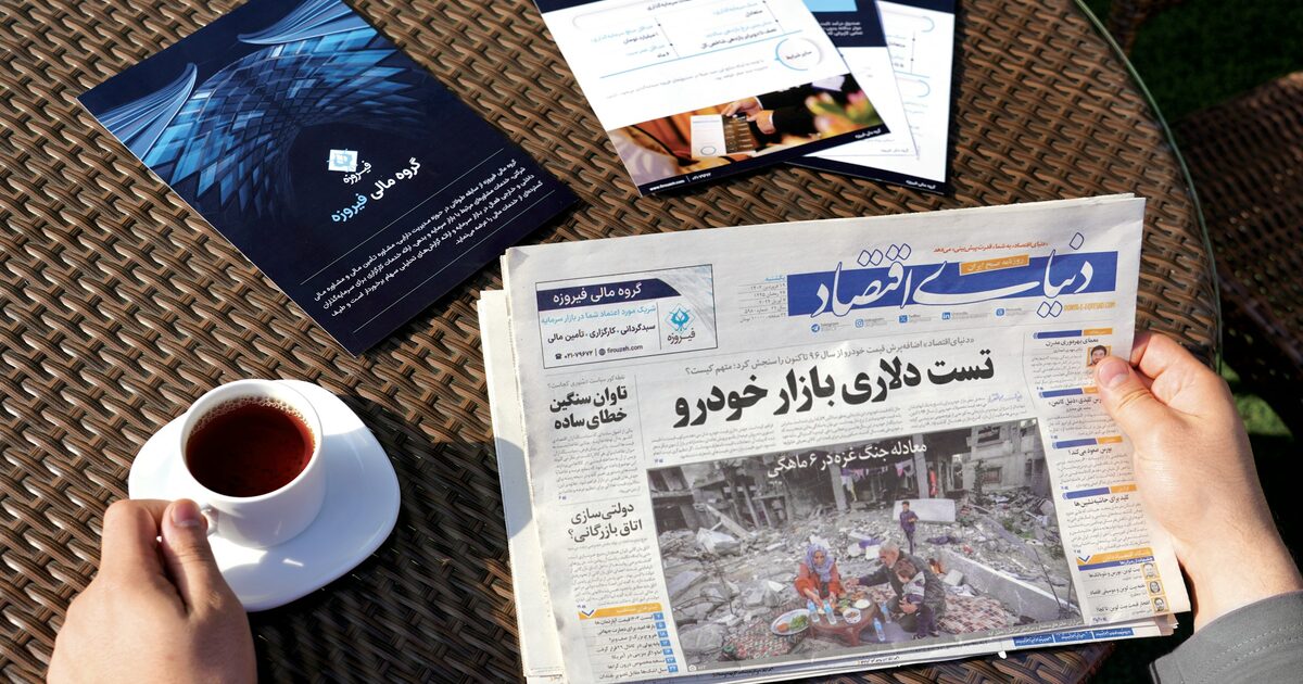 A person sitting at a table reading a folded newspaper