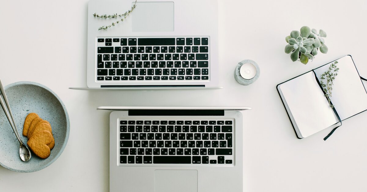 Two silver laptop computers open side by side on a desk